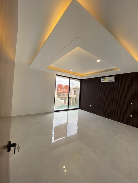 Modern empty apartment interior with geometric ceiling design, ambient lighting, polished white floor, and dark wood accent wall.