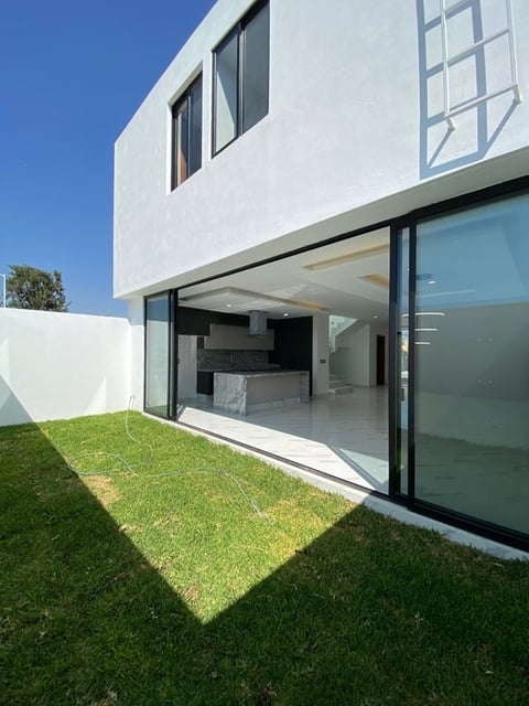 Modern white two-story house with large sliding glass doors, green lawn, and clear blue sky