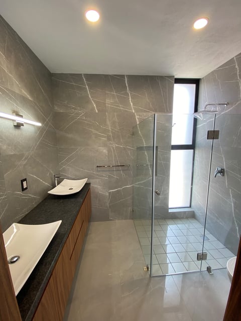 Modern bathroom with gray marble tiles, floating wooden vanity with white vessel sinks, frameless glass shower enclosure, and recessed ceiling lights