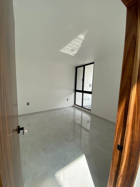 Empty room with white walls, polished gray floor, black-framed window, wooden door frames, and natural light from skylights
