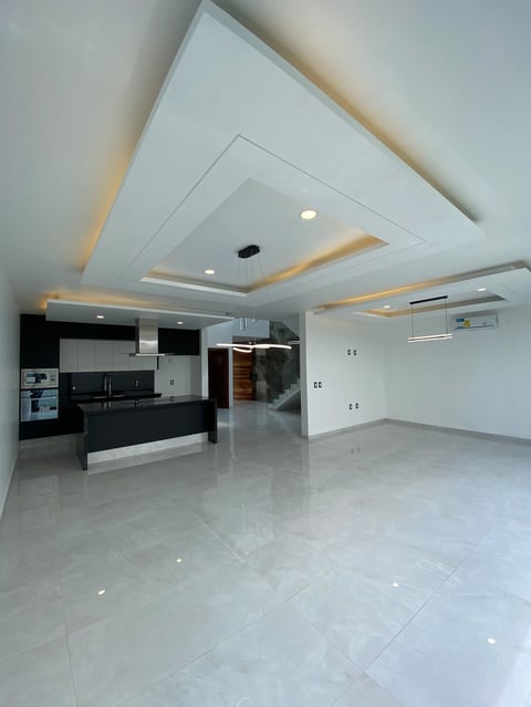 Modern open-plan kitchen and living room with white ceiling features, black kitchen cabinetry, polished white floor tiles, and recessed lighting