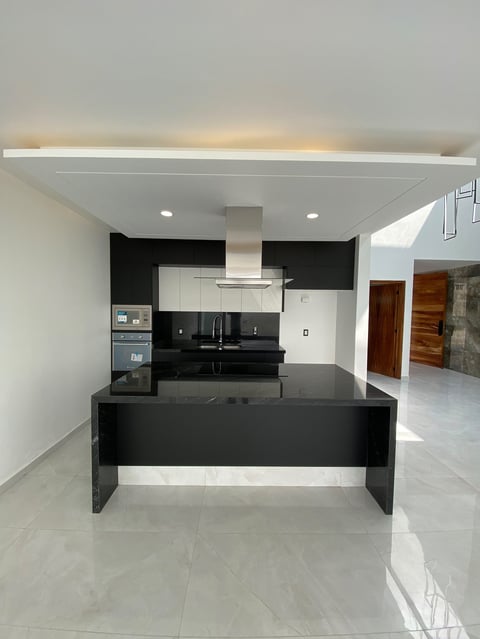 Modern kitchen with black and white color scheme, central island, stainless steel appliances, and skylight ceiling