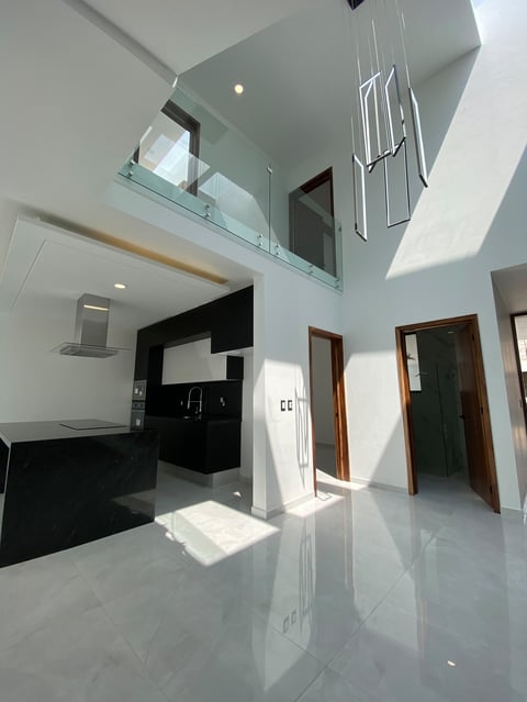 Modern two-story open-plan interior with white flooring, black kitchen, mezzanine level with glass railing, and wooden doorways
