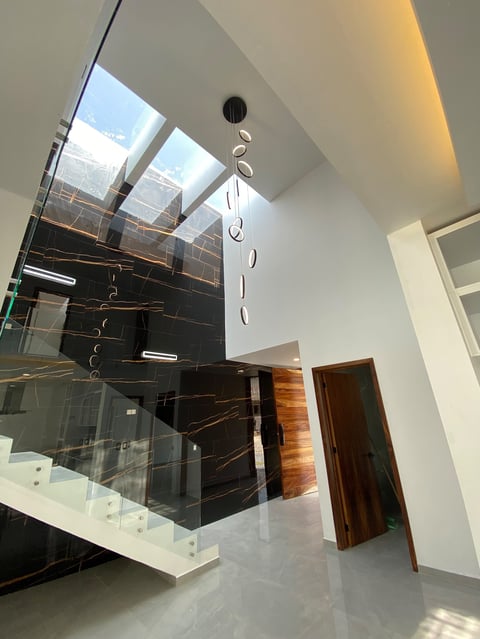 Modern interior staircase with black marble steps, glass railings, and skylights illuminating the two-story atrium space