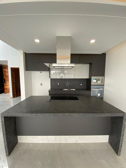 Modern kitchen with dark gray island countertop, stainless steel range hood, and black cabinetry with white accents
