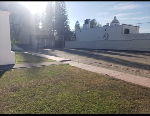 RV parked beside white building with green lawn and trees in morning sunlight