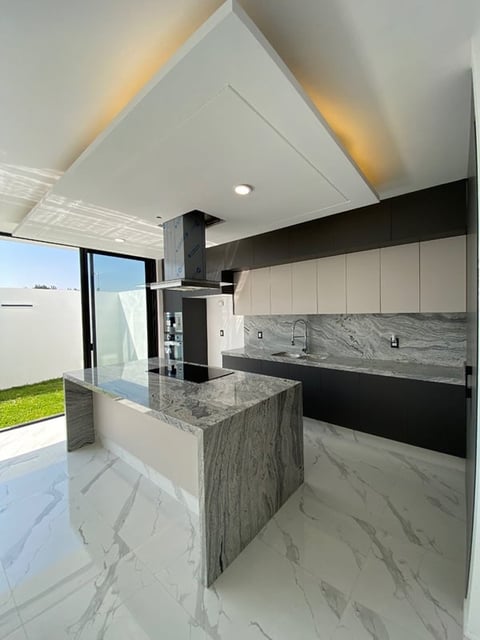Modern kitchen with gray marble countertops, white and black cabinetry, central island, and angular white ceiling with accent lighting