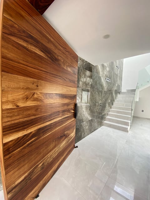 Modern entrance hallway with rich wooden door on left, gray textured wall, white ceiling, and staircase visible in background