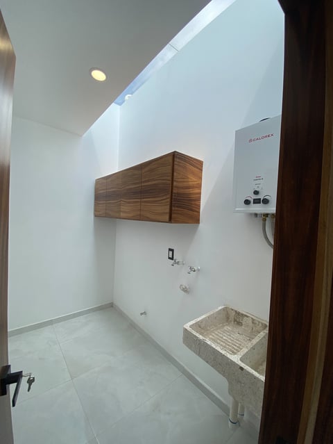Modern bathroom with white walls, wooden cabinet, water heater, and concrete sink