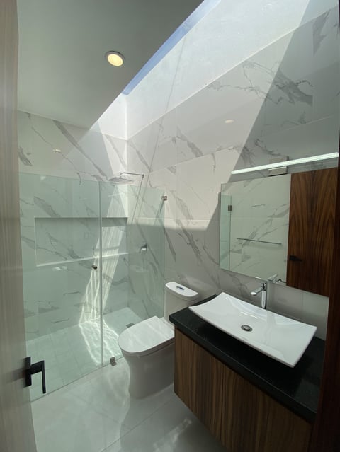 Modern bathroom with marble shower enclosure, white vessel sink, wooden vanity, and skylight above