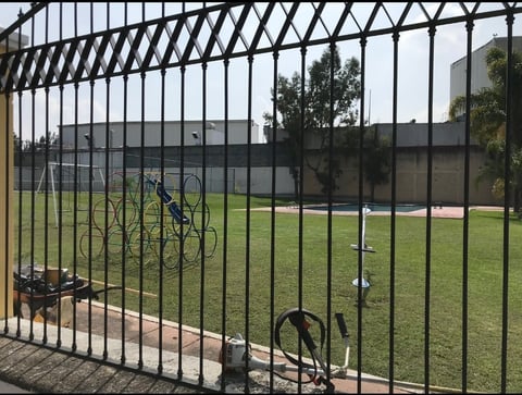 Black metal fence with bikes leaning against it in front of a green sports field and trees