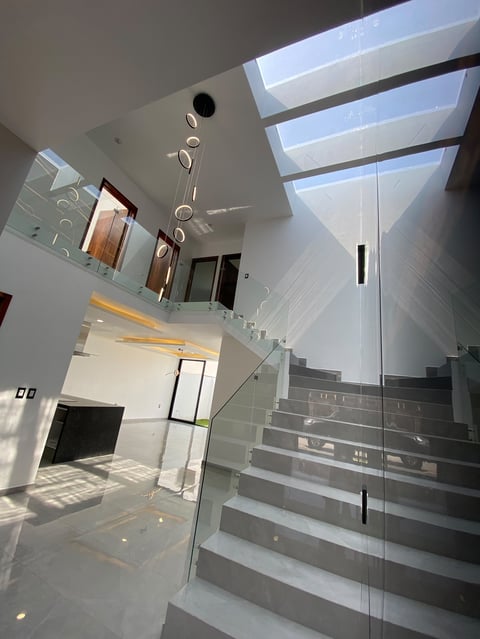 Modern interior staircase with glass railing, skylights, and contemporary fixtures in a bright white minimalist space