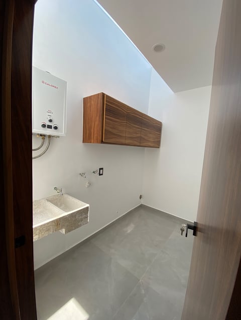 Modern bathroom with concrete floor, wall-mounted wood cabinet, stone sink, and white water heater on wall