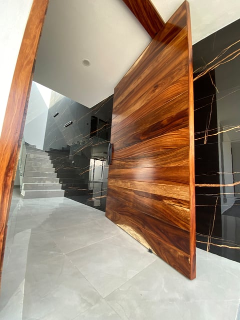 Modern entryway with an open wooden door featuring rich grain patterns, leading to a hallway with dark stairs and minimalist design.
