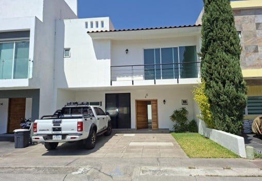 Modern white two-story house with a white pickup truck parked in the driveway, green landscaping, and contemporary architecture