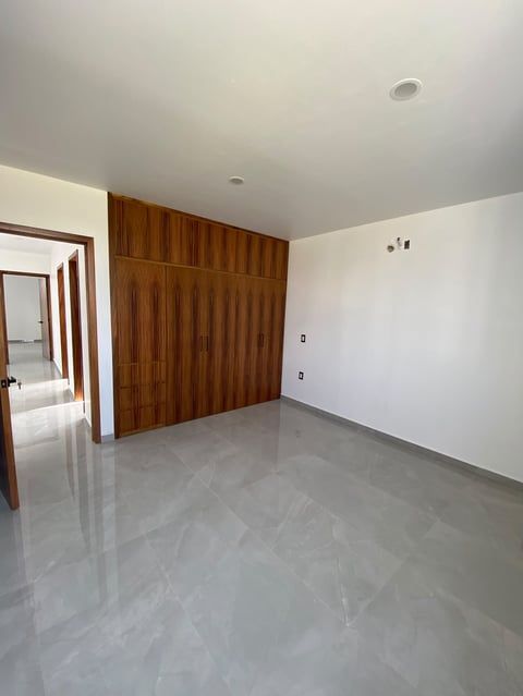 Empty room with polished gray tile floor, white walls, wooden closet door, and ceiling lights