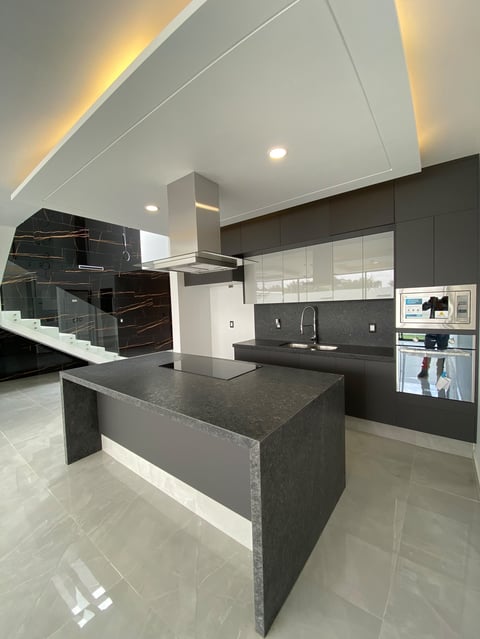 Modern kitchen with dark gray island, sleek cabinetry, stainless steel hood, and ambient ceiling lighting