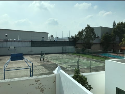 Rooftop recreational area with tennis courts, basketball hoop, and seating surrounded by industrial buildings and trees