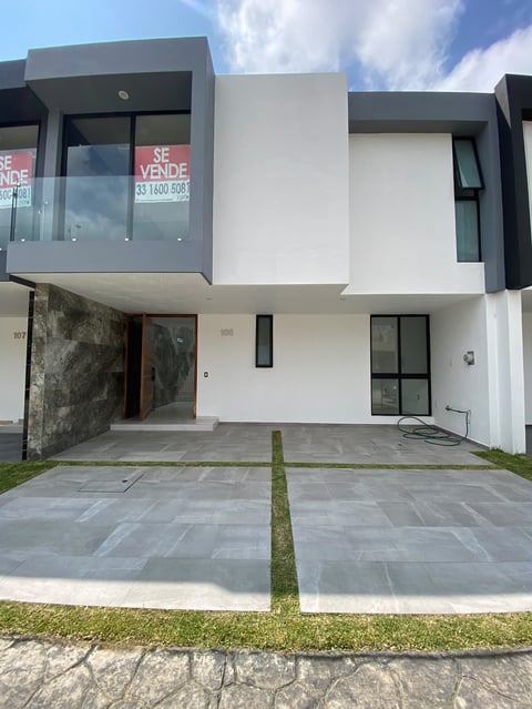 Modern two-story residential townhouse with white and gray facade, glass windows, and paved courtyard under blue sky