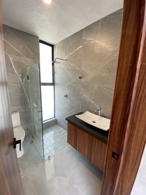 Modern bathroom with gray marble walls, glass shower enclosure, wooden vanity with white sink, and white tile flooring