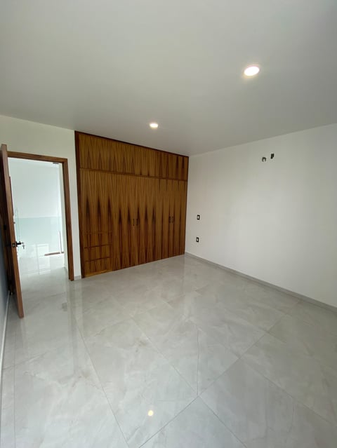 Empty modern bedroom with polished gray floor, wooden wardrobe, open door, and white walls with recessed lighting