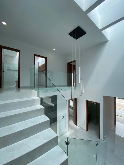 Modern minimalist staircase with white steps, glass railings, and skylights in a contemporary home interior