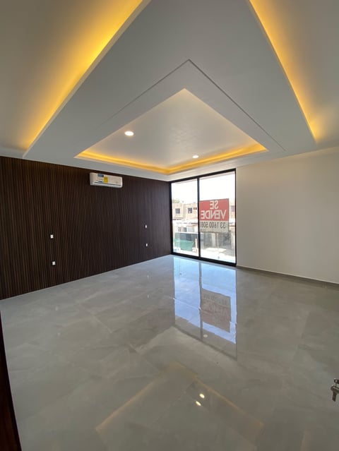 Modern empty commercial space with polished concrete floor, dark accent wall, geometric ceiling with warm LED lighting, and glass storefront window