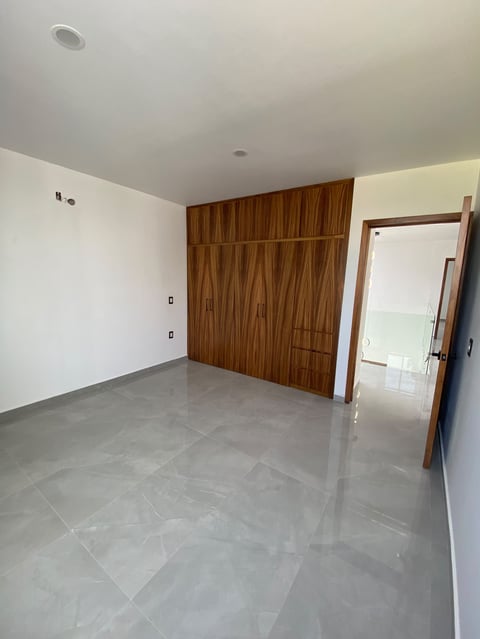 Empty interior room with gray tiled floor, white walls, wooden feature wall, and open doorway to adjacent space
