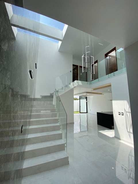 Modern two-story open interior with floating staircase, glass railings, skylights, and minimalist white and gray design