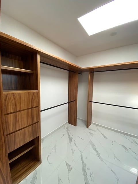 Modern walk-in closet with wooden cabinetry, white walls, marble flooring, and skylight illumination