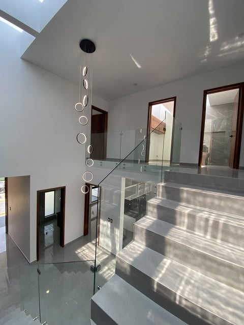 Modern multi-level interior with floating staircase, glass railings, circular pendant light, and skylight in minimalist white space