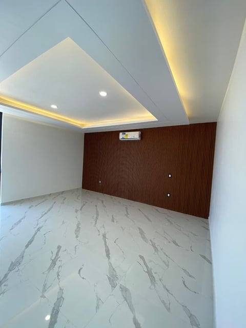 Empty modern interior room with geometric ceiling lights, dark wood accent wall, and marble-patterned flooring