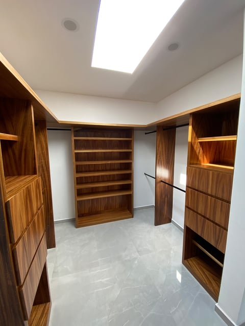 Modern walk-in closet with wood cabinetry, shelving, and polished concrete flooring under bright ceiling lights
