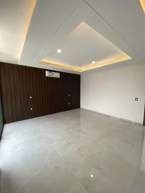 Empty modern room with polished floor, dark wood accent wall, recessed ceiling lights, and geometric ceiling design
