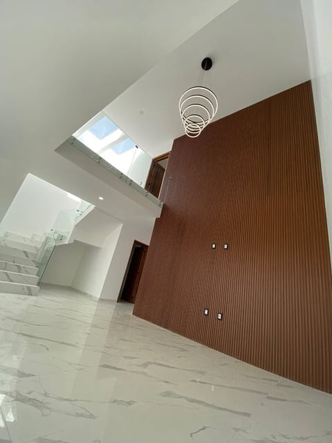 Modern hallway with white ceiling, marble floors, brown wood panel wall, skylight, spiral light fixture, and staircase