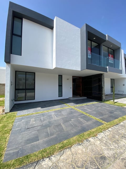 Modern two-story house with white and dark gray exterior, black windows, and dark stone driveway under clear blue sky