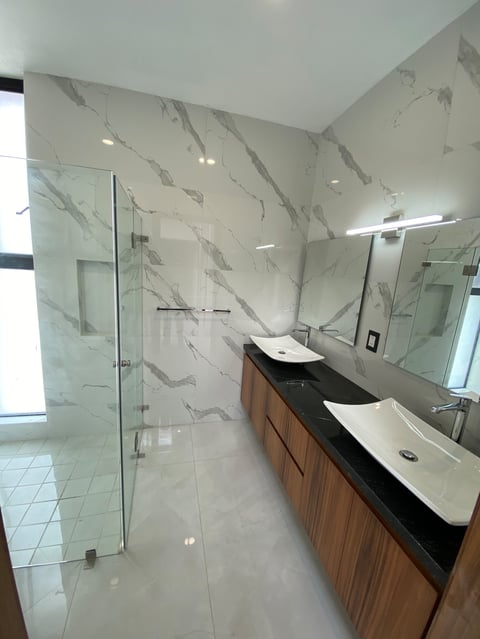 Modern bathroom with marble tile walls, walk-in shower with glass enclosure, double vanity with wooden cabinets and white vessel sinks