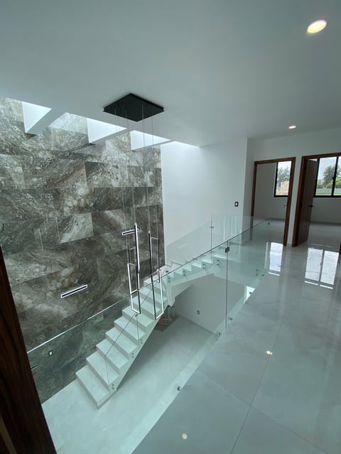 Modern bathroom with floating glass staircase, stone-tiled walk-in shower, and polished white floor with natural lighting