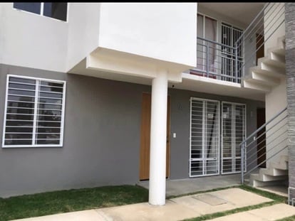 Modern gray and white residential house with wood door, metal window grilles, small lawn, and concrete entryway