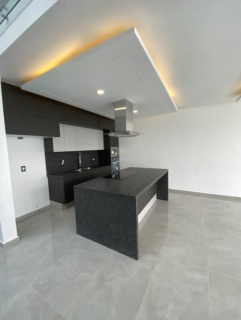 Modern kitchen with black and white cabinetry, dark island, stainless steel range hood, and warm ceiling lighting